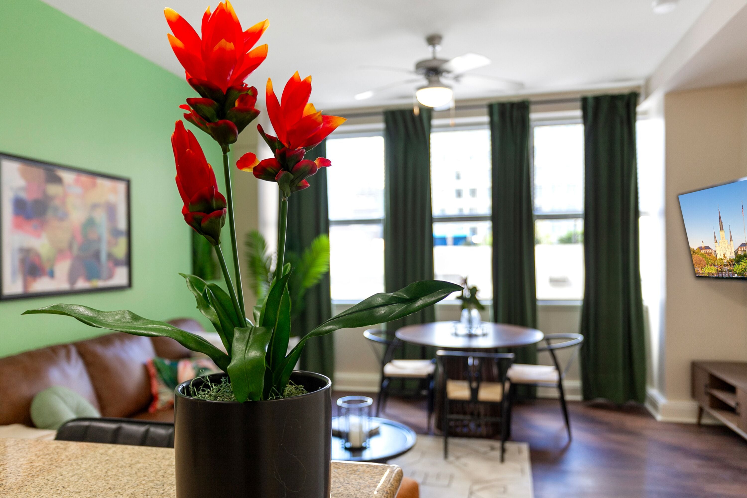 A living room with a potted plant, a brown leather couch, a dining area with a table and chairs, and a ceiling fan.
