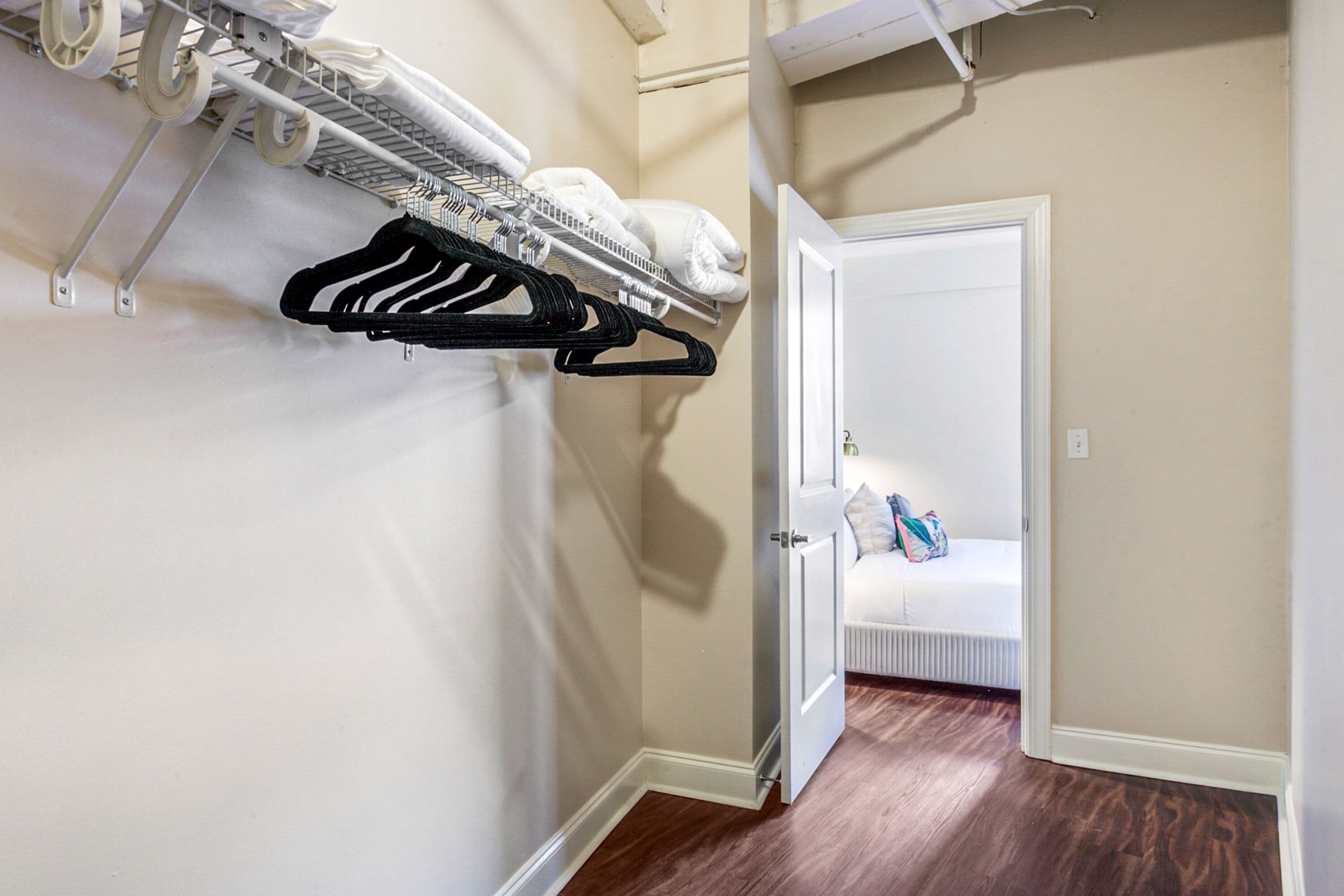Un pasillo con un perchero, una cama con almohadas y una puerta que da a otra habitación.