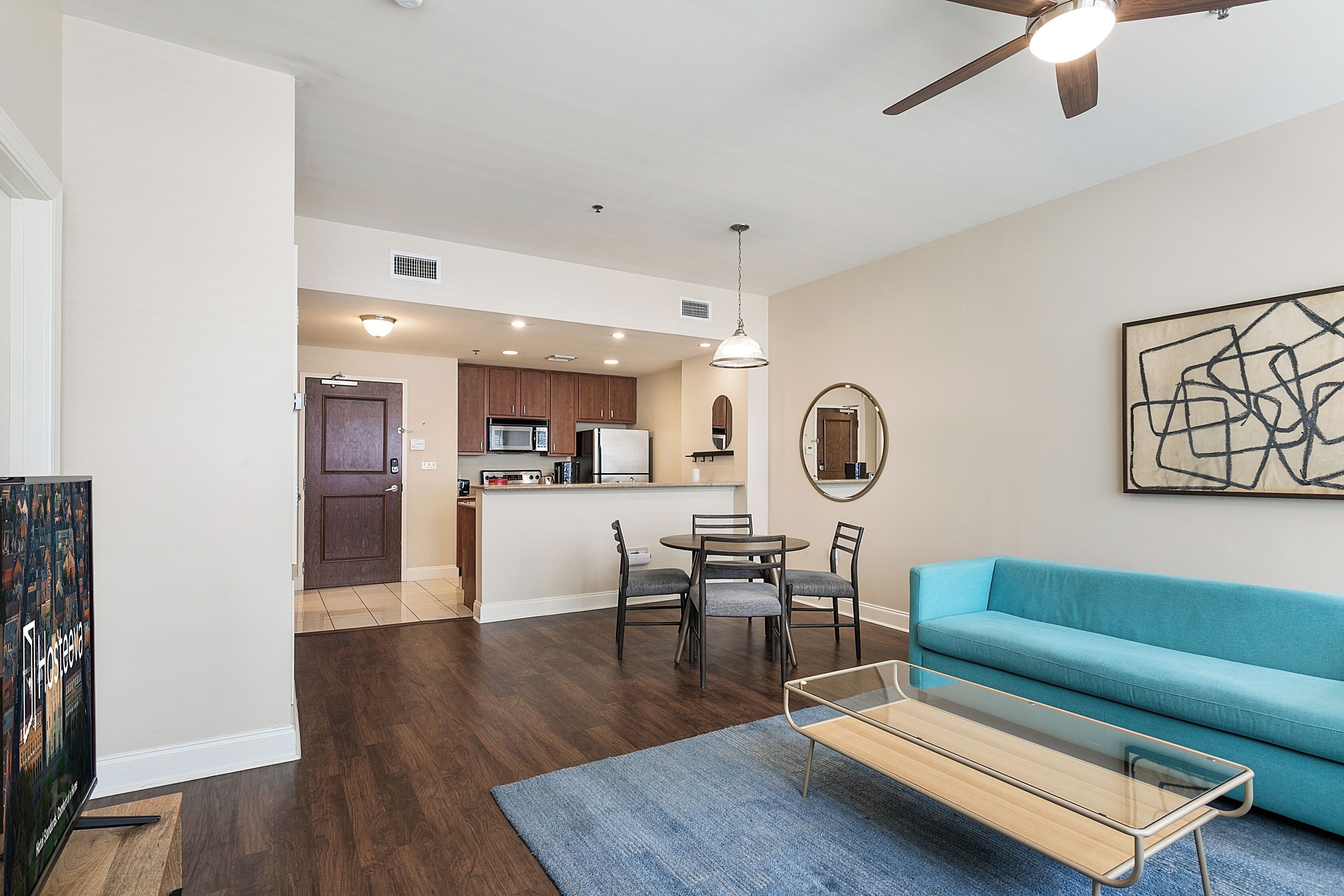 A modern living room with a blue sofa, a glass coffee table, and a dining area with chairs and a table.