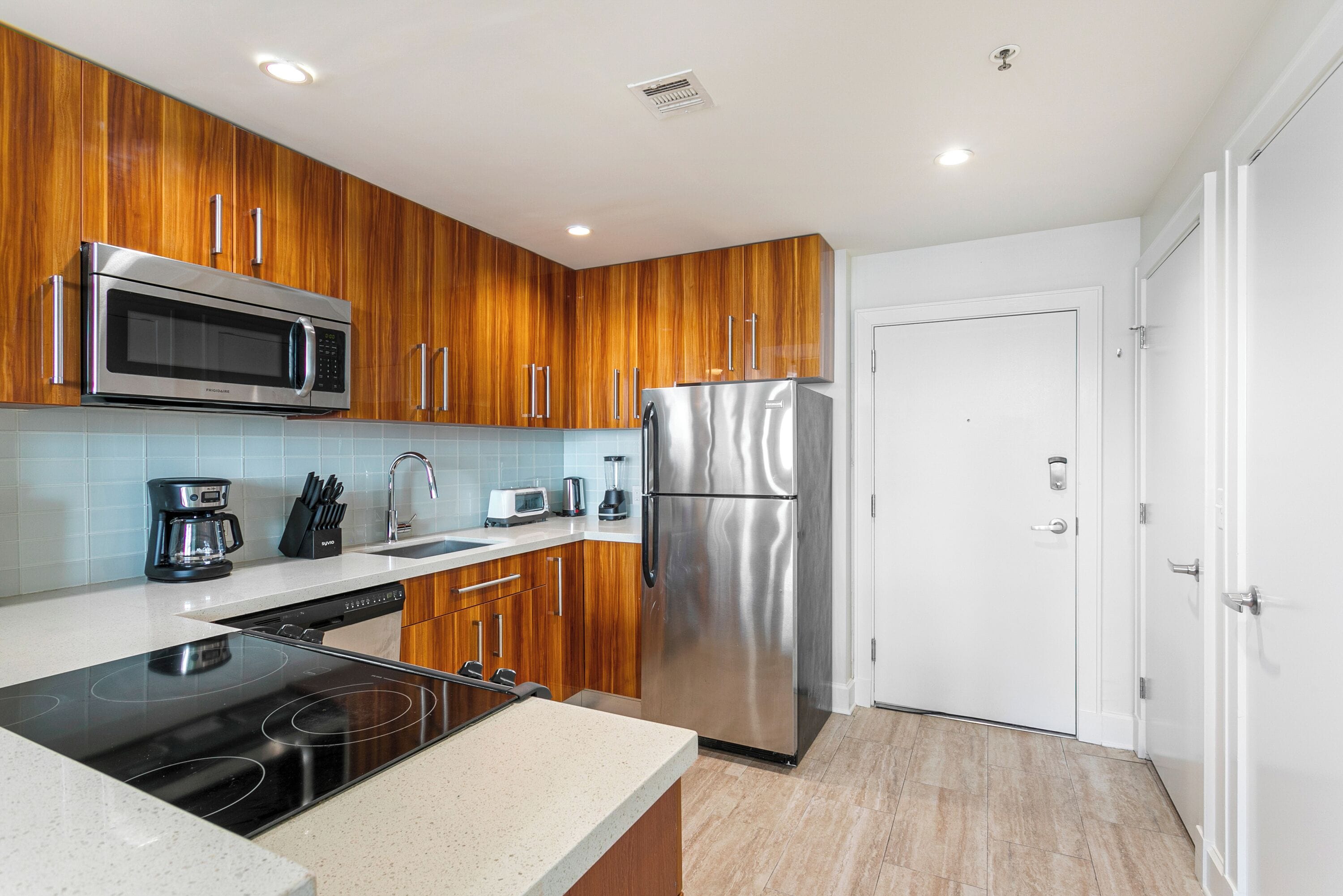 A modern kitchen with wooden cabinets, stainless steel appliances, and a white door.