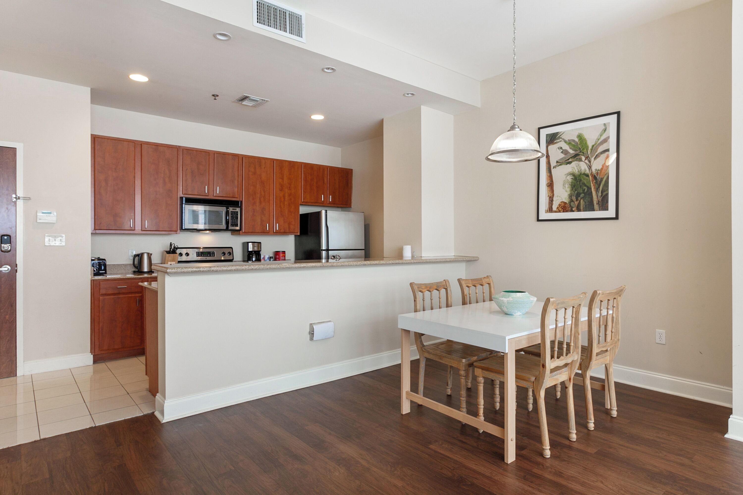 Una cocina moderna con armarios de madera, un microondas y un refrigerador. Hay una mesa de comedor con sillas y una lámpara colgante.