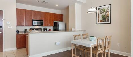 Una cocina moderna con armarios de madera, un microondas y un refrigerador. Hay una mesa de comedor con sillas y una lámpara colgante.