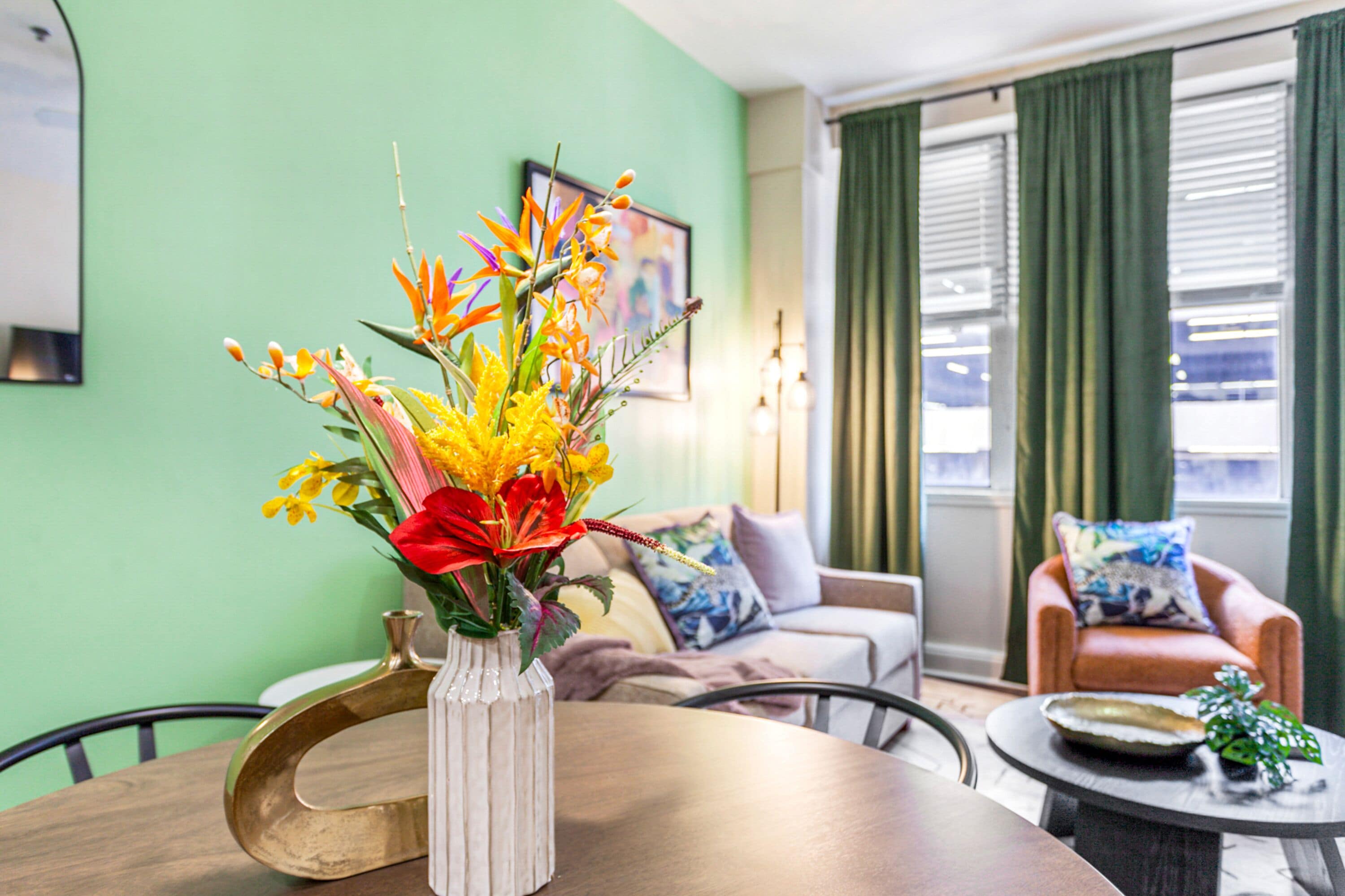 A living room with a round table, a vase with flowers, a sofa, and a chair.