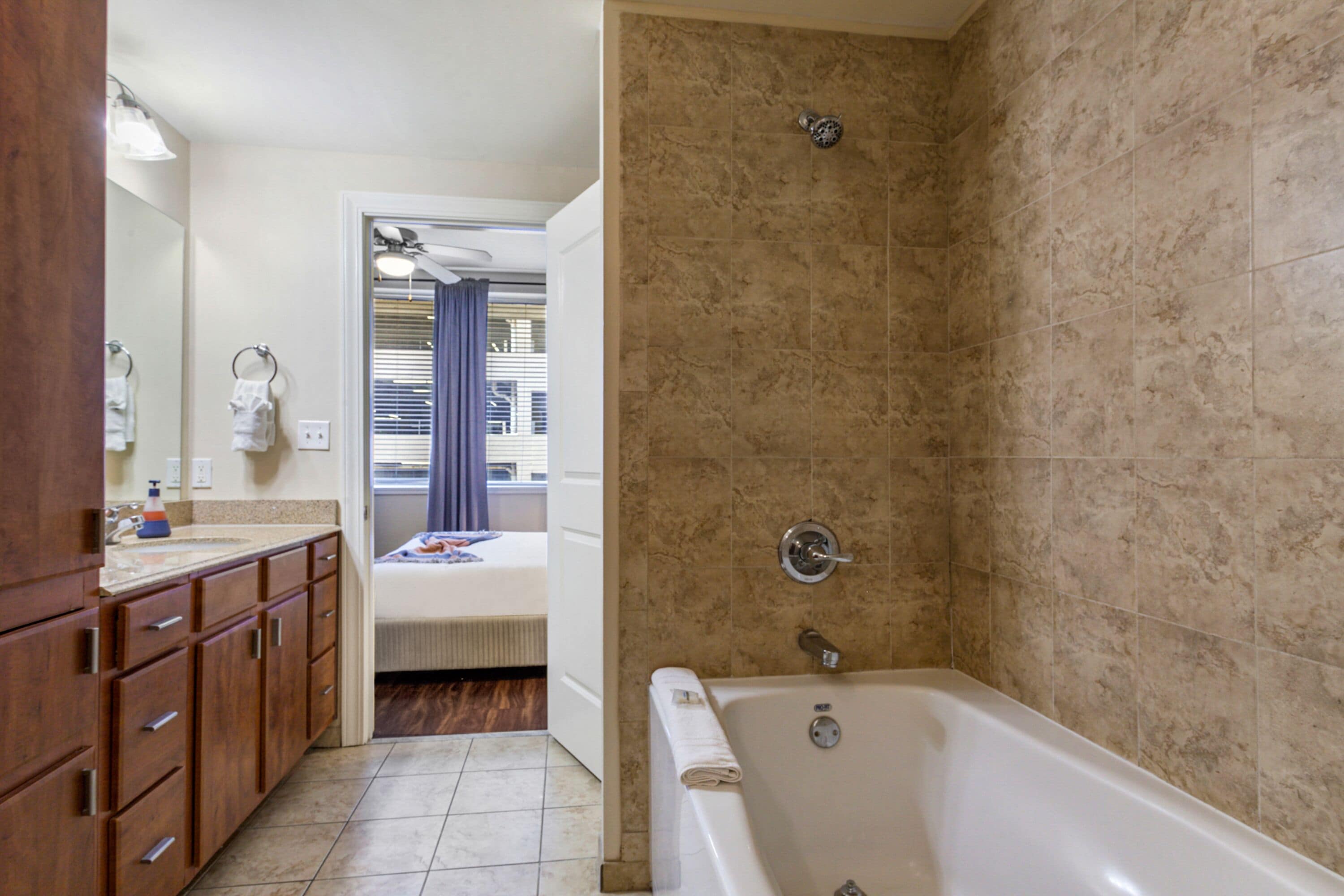 A bathroom with a bathtub, a sink with a mirror, wooden cabinets, and a shower area.