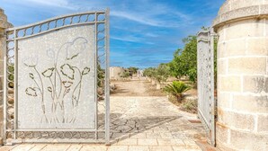 A stone pathway leading to a gated entrance with a decorative metal gate featuring floral designs. - Country House 'Il Papavero Rosso - Cozy Villa' with Private garden and Wi-Fi (Gagliano del capo)