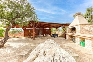 Une terrasse extérieure dotée d’un espace barbecue en pierre, d’une pergola en bois et de coins salon.