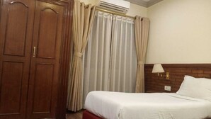 A hotel room with a bed, a wardrobe, curtains, an air conditioning unit, and a wall-mounted lamp. - Club Jawai (Butwal)