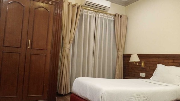 A hotel room with a bed, a wardrobe, curtains, an air conditioning unit, and a wall-mounted lamp.