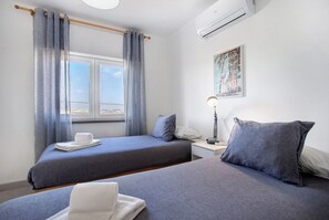 Een hotelkamer met twee bedden, een raam met gordijnen, een nachtkastje met een lamp en een airconditioning.