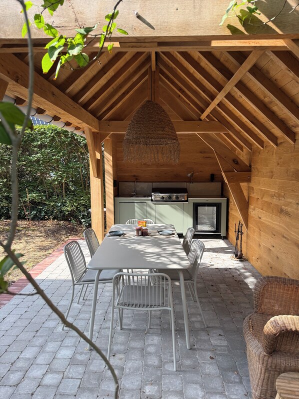 A covered outdoor patio with a dining table, chairs, and a kitchen area.