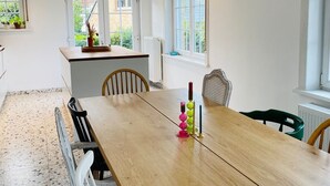 Moderni keittiö, jossa on puinen ruokapöytä, tuolit ja katosta roikkuva valaisin.