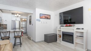 Un salon moderne avec une cheminée, un téléviseur et un coin repas comprenant des chaises et une table.