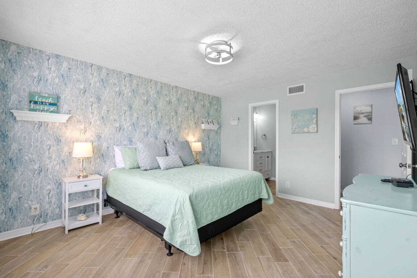 Une chambre à coucher comprenant un lit, des lampes de chevet, une commode et un mur orné d’un motif texturé.