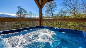 A hot tub with a wooden deck and metal railing, surrounded by trees and mountains. - Timeless View, Mountain Views, Hot Tub, WIFI, Game Room, Free Attraction Tickets (Sevierville)