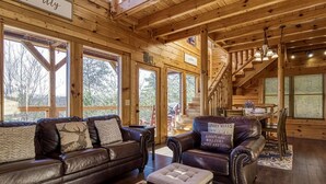 A cozy cabin interior with a wooden staircase, leather sofas, and a dining area. - Timeless View, Mountain Views, Hot Tub, WIFI, Game Room, Free Attraction Tickets (Sevierville)