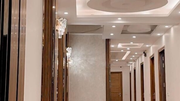A hallway with a polished tile floor, recessed lighting, and a central chandelier. - Hotel The Palm View (New Delhi)
