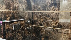 A bathroom with a white toilet, a sink, and a shower area with a marble wall. - Hotel The Palm View (New Delhi)