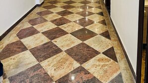 A hotel hallway with a checkered floor pattern, a modern ceiling design, and a door at the end. - Hotel The Palm View (New Delhi)