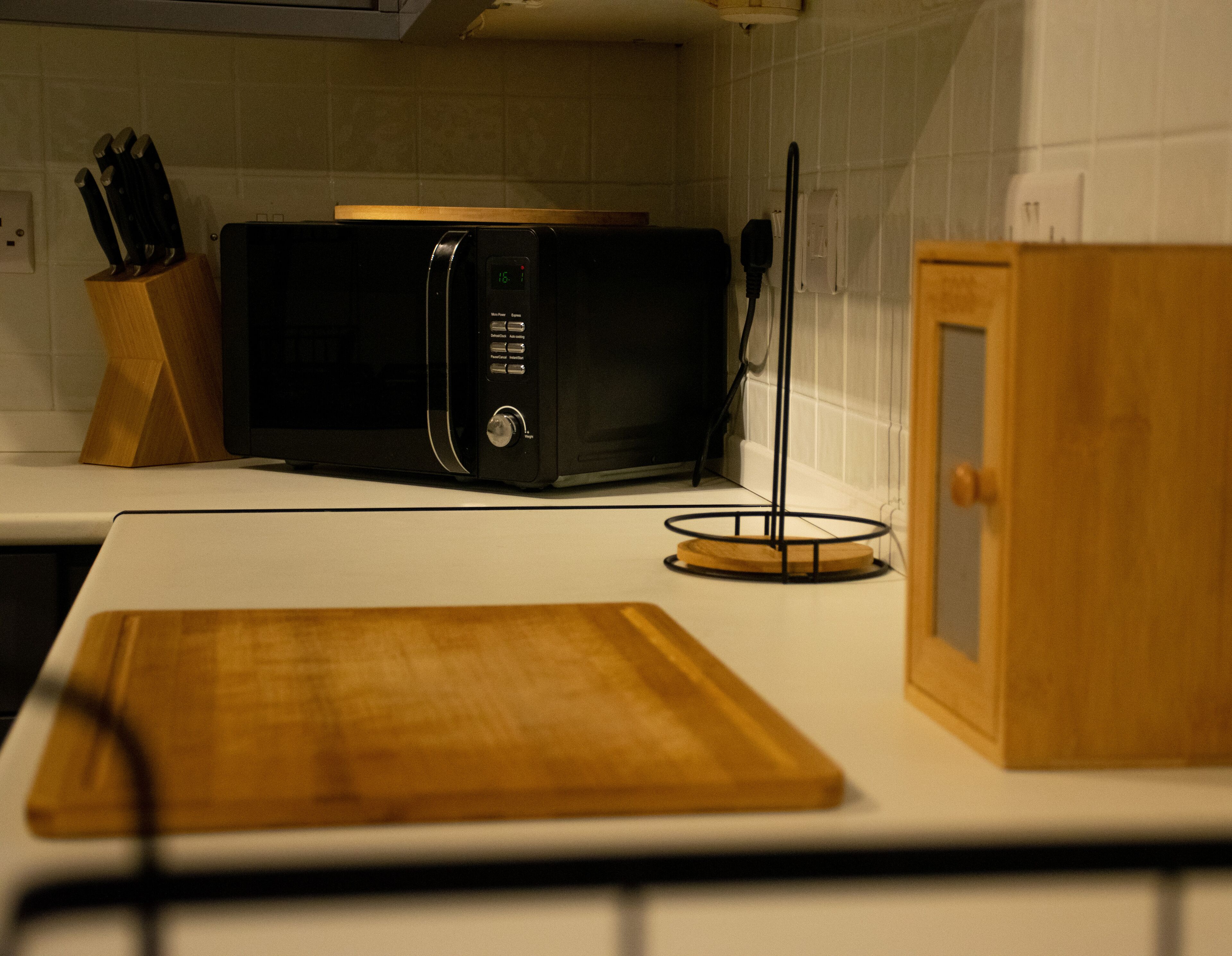 Una cocina con microondas, tabla de cortar de madera y bloque de cuchillos.