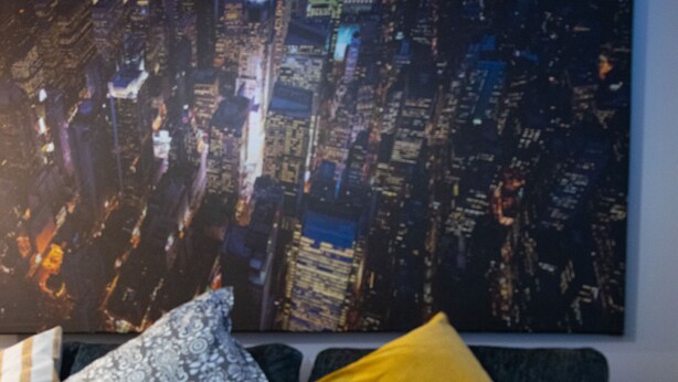 A modern living room with a dark sofa, patterned cushions, and a cityscape painting on the wall.