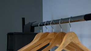 A clothing rack with wooden hangers against a wall with a window.