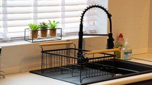 A kitchen with a washing machine, a sink with a dish rack, and a window with blinds.
