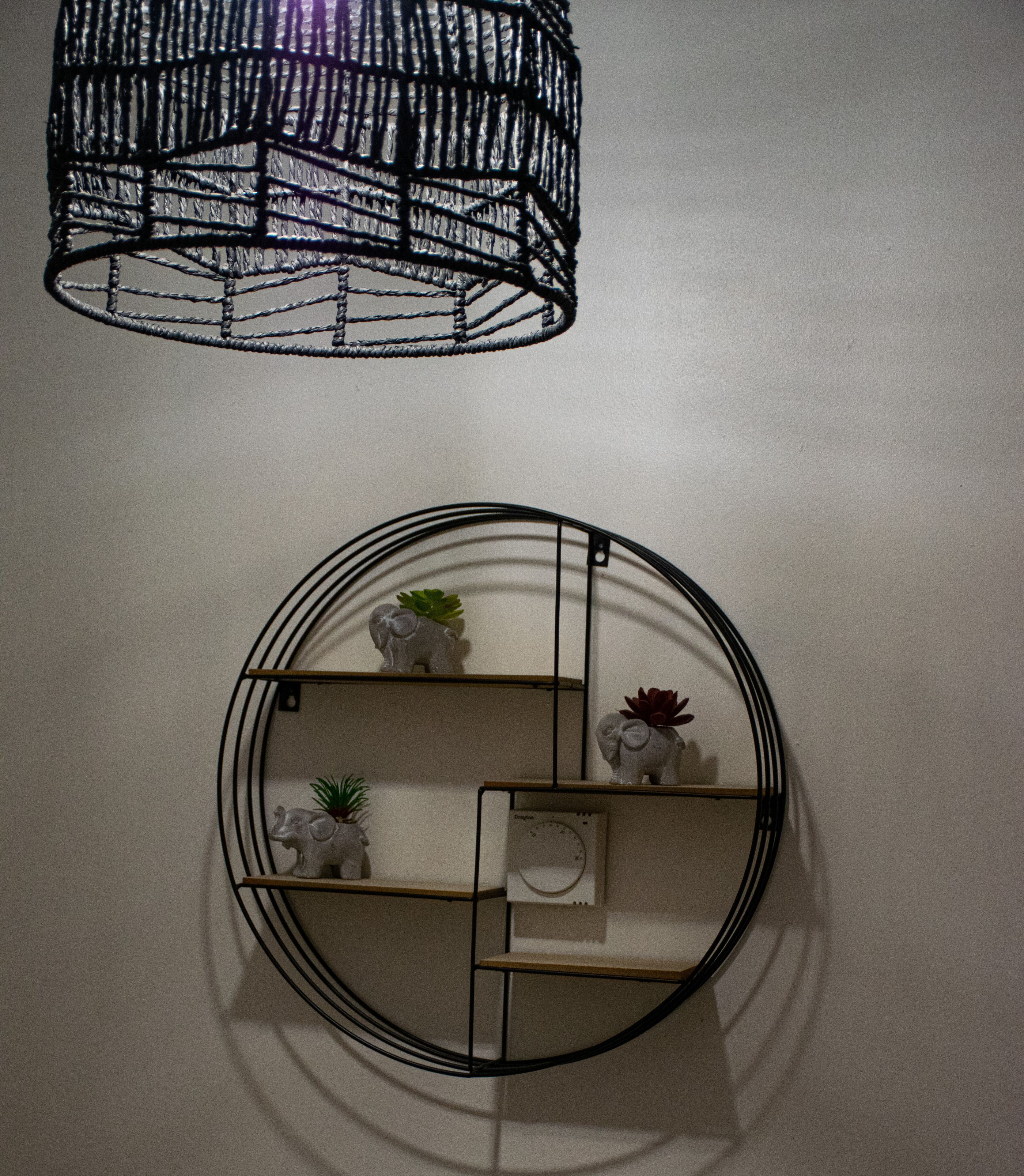 Un estante circular de pared con varios compartimentos, cada uno con objetos decorativos y una pequeña planta.