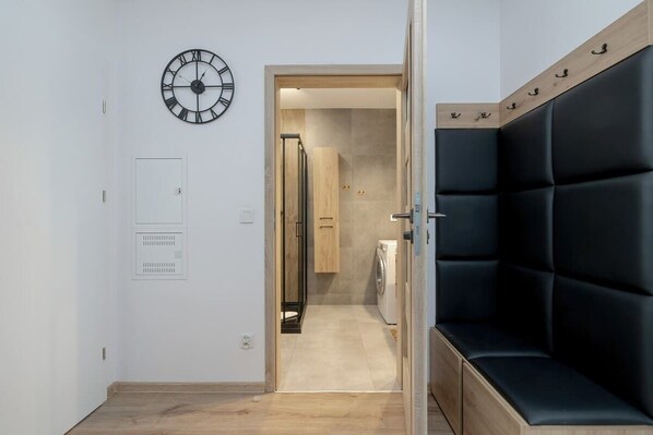 Un interior moderno con un banco de cuero negro, un reloj de pared y un área de lavandería visible.