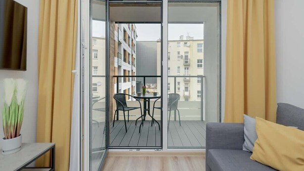 Un apartamento moderno con balcón, un sofá y una pequeña mesa con sillas.