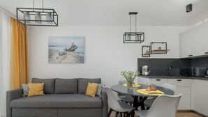 Una sala de estar moderna con un sofá gris, una mesa de comedor con sillas y una cocina con armarios blancos y encimera negra.