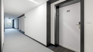Un pasillo moderno con suelo alfombrado, una puerta numerada 225 e interruptor de luz en la pared.