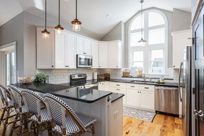 Une cuisine moderne avec des meubles blancs, un grand îlot central, des appareils en acier inoxydable et des chaises en osier.