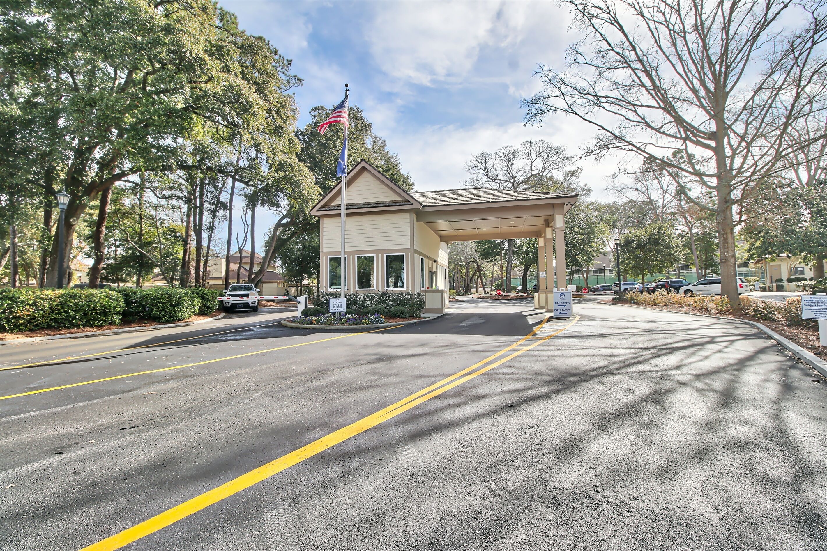 A small building with a covered entrance, surrounded by trees and parked cars.