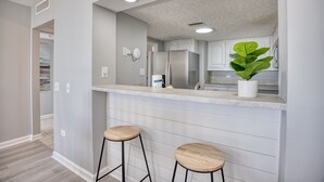 Eine moderne Küche mit weißen Schränken, einem Edelstahlkühlschrank und einem Topf mit Pflanze auf der Arbeitsplatte.