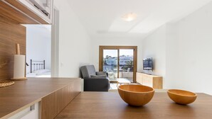 A modern living room with a wooden dining table, two wooden bowls, a grey sofa, and a balcony with a view of the city. - Cozy apartment in Orihuela with WiFi (Orihuela)