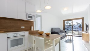 A modern kitchen with white cabinets, a wooden countertop, and a built-in oven. There is a dining area with a table and chairs, and a gray sofa. The room has large windows with a view of palm trees and buildings. - Cozy apartment in Orihuela with WiFi (Orihuela)