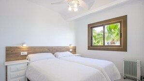 A bedroom with two beds, a wooden headboard, bedside lamps, a window with a view of palm trees, and a radiator. - Cozy apartment in Orihuela with WiFi (Orihuela)