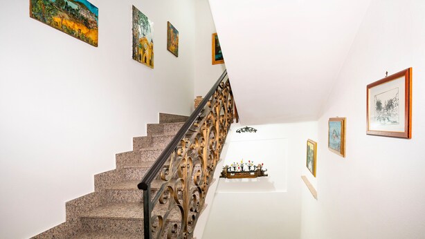 Un escalier orné de rampes en métal ouvragé et de marches en granit, menant à un palier avec un mur blanc et des œuvres d’art encadrées.