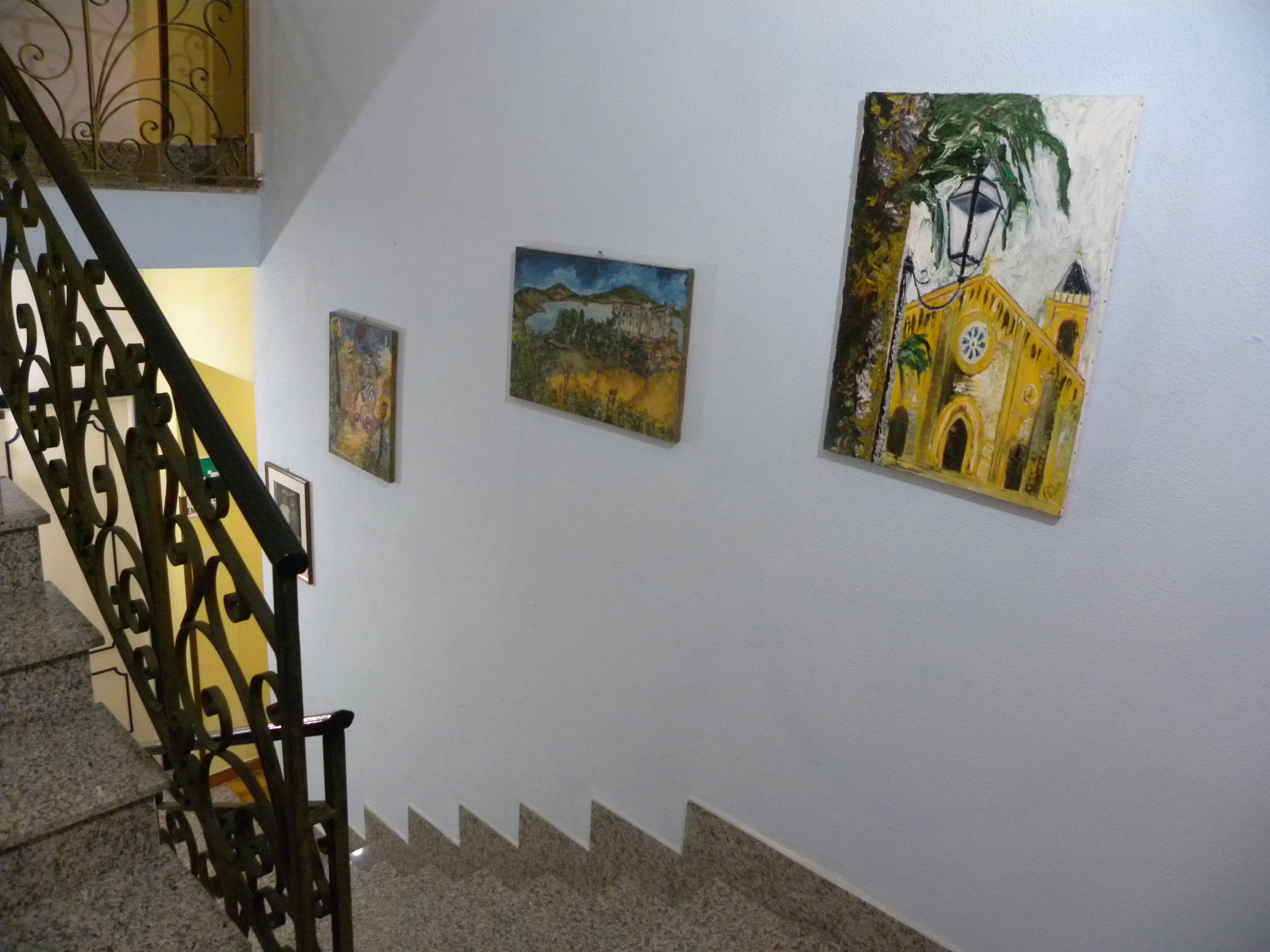 A staircase with a metal railing leading to a landing where three paintings are displayed on the wall.