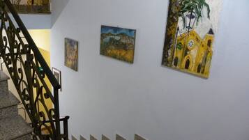 A staircase with a metal railing leading to a landing where three paintings are displayed on the wall.