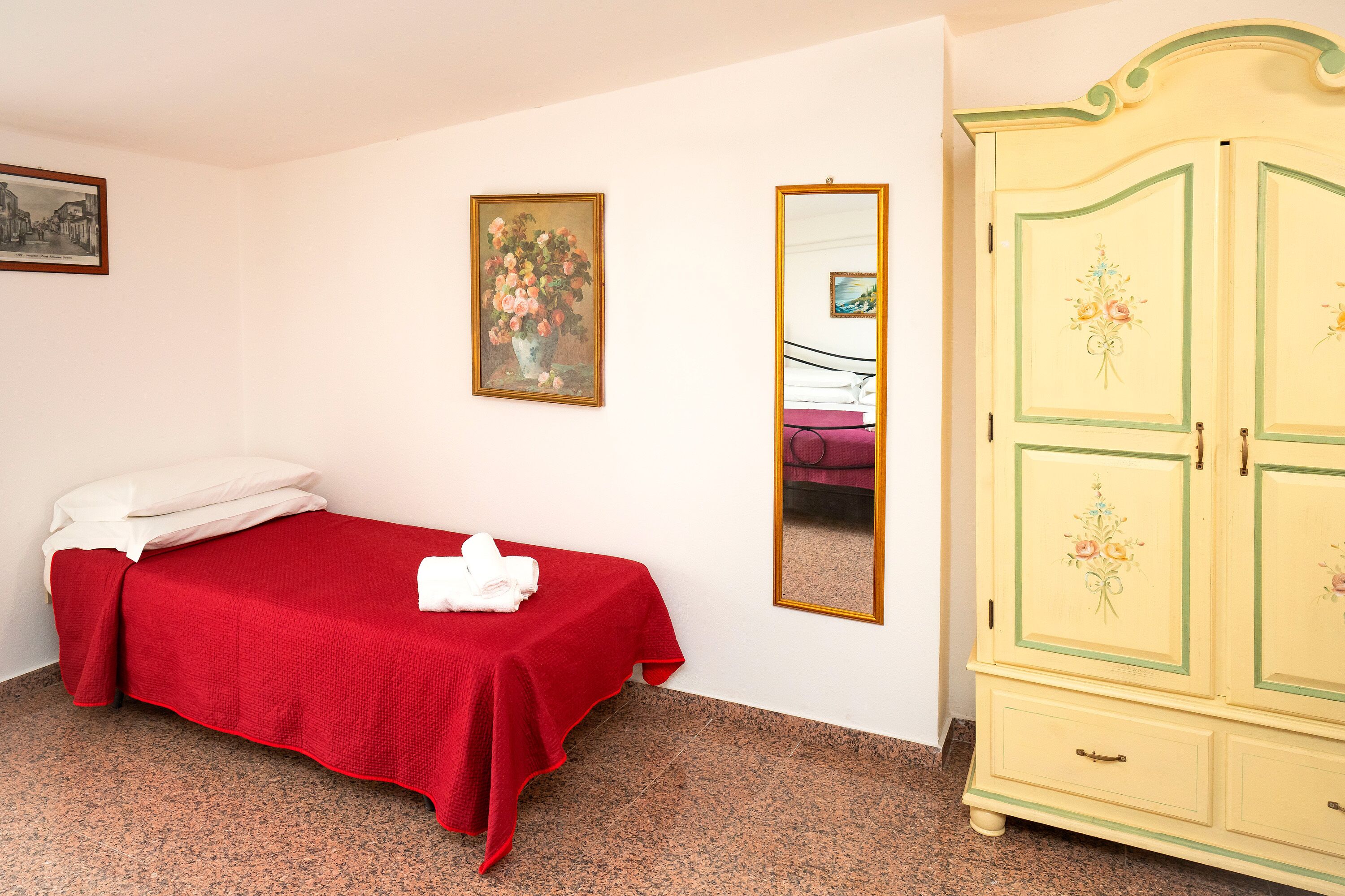 Quarto com cama, guarda-roupa, espelho e duas imagens emolduradas na parede.