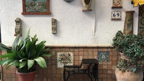 Une terrasse avec un mur recouvert de carreaux, une machine à coudre et des objets décoratifs, notamment un vase et un tableau encadré.