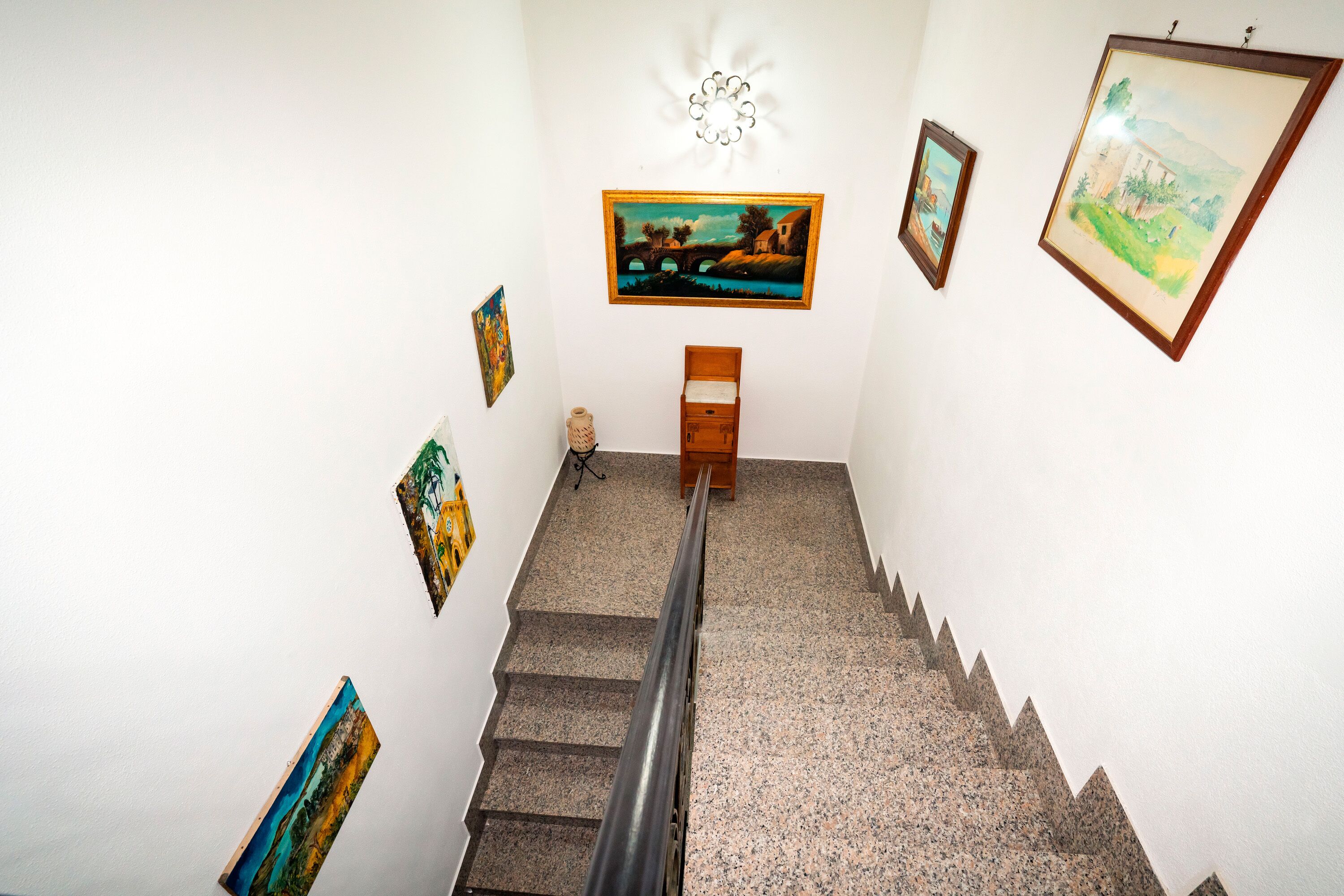 A staircase with artwork on the walls, a wooden bench, and a light fixture.