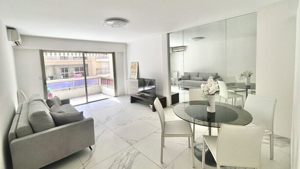 A modern living room with a sofa, a glass dining table, and a TV.