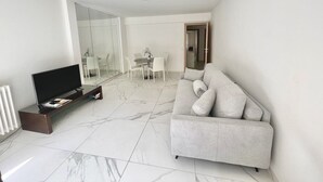 A modern living room with a flat-screen TV, a sofa, a dining table with chairs, and a glass partition.
