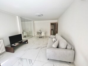 Un salon moderne doté d’un téléviseur à écran plat, d’un canapé, d’une table à manger avec des chaises et d’une cloison en verre.