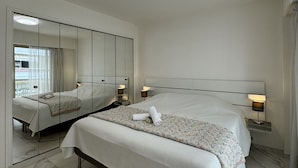 A hotel room with a large bed, a bedside table with a lamp, a mirror, and a ceiling light.