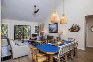 Un coin repas avec une table bleue, des chaises en osier et des lampes suspendues.