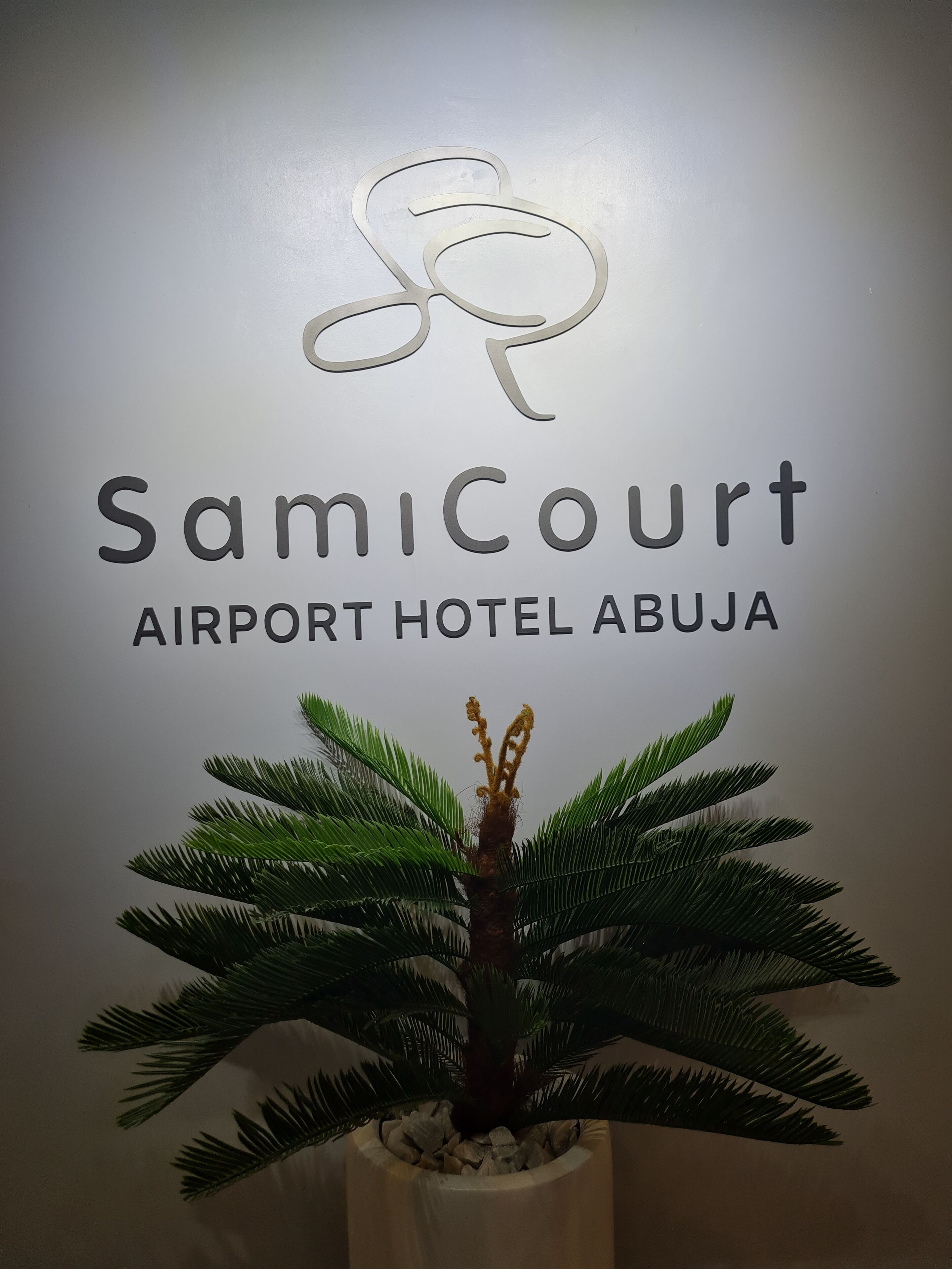 A sign for Samicourt Airport Hotel Abuja with a logo and name.
