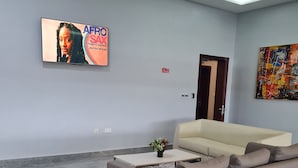 A modern waiting area with a sofa, a coffee table, a patterned rug, a TV screen, and a colorful abstract painting. - Sami Court Airport Hotel Abuja (Abuja)